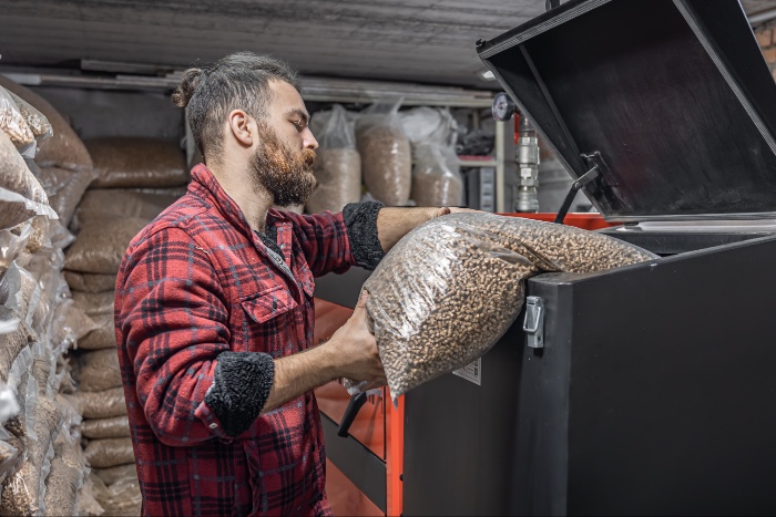 Man loading wood pellets into a biomass boiler